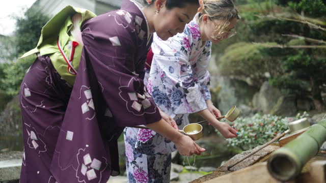 Female friends purifying hands at “Chozusha” in temple - side view