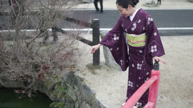 Woman in kimono looking at carps in pond in temple - slow motion