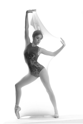 Beautiful ballerina dancing on light grey background. Dark silhouette of dancer