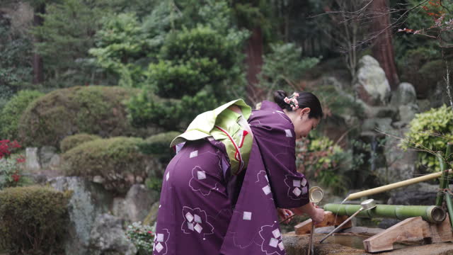 Female friends purifying hands at “Chozusha” in temple - side view
