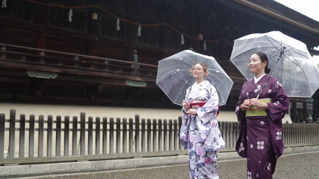 Women in kimono walking beside the main hall of temple in a rainy day - low angle view