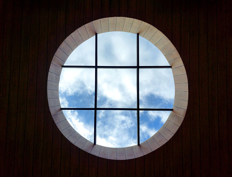 Circular lightwell from rumber ceiling rooftop as a main skylight showing sky above. With black metal framings and transparant glass panel.