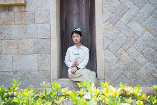 A young Latina woman in a black dress and backpack explores the colorful grounds of Deoksugung Palace in Seoul, South Korea, smiling as she enjoys her visit.