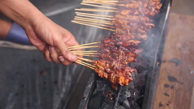 Satay grilled while holding a hand fan