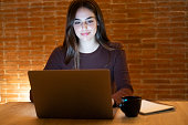 Beautiful Authentic Young Woman Sitting at a Table in Cozy Kitchen and Using Laptop Computer at Home at Night. Female Smiling and Chatting on the Internet and Social Media, Doing Online Research.