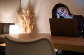 Young pretty smiling woman using laptop in home at night. Happy girl looking at computer. Cheerful people sitting at desk in living room. Concept of enterprising, telecommuting and hardworking person.