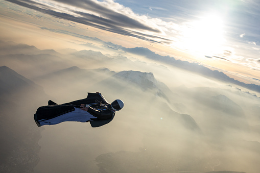 Aerial view of inverted wingsuit flier soaring over mountainous landscape at sunset