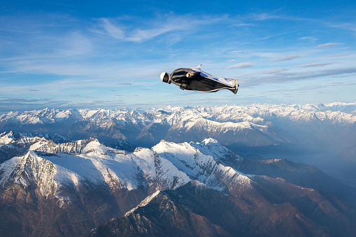 Wing suit flier soars above mountain landscape, blue sky day