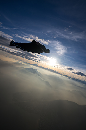 Wing suit flier soars above mountain landscape at sunset