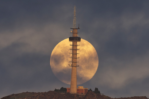A large full moon rising behind an antenna tower on Mount Mendibil, Bizkaia, moments before sunset