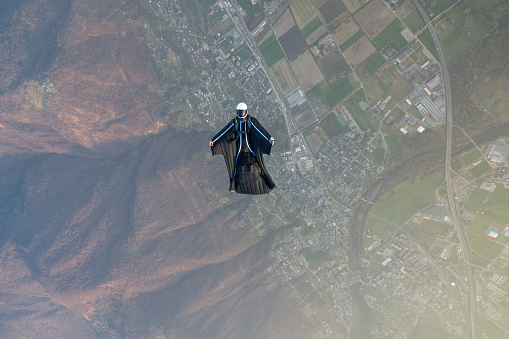 Aerial view of inverted wingsuit flier soaring over agricultural land and mountainous landscape