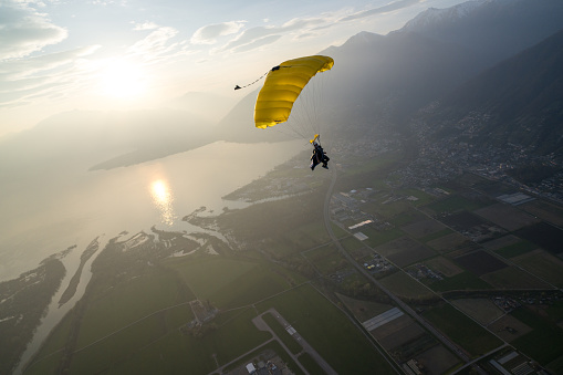 Wingsuit flier parachutes down to valley and lake at sunset