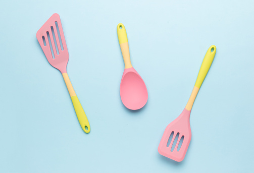 Yellow and pink silicone kitchen spatulas on a blue background. Creative kitchen utensils.