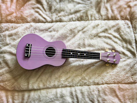 Ukulele made from wood  in purple color put on soft cloth background,Hawaiian acoustic instrument,blurry light around