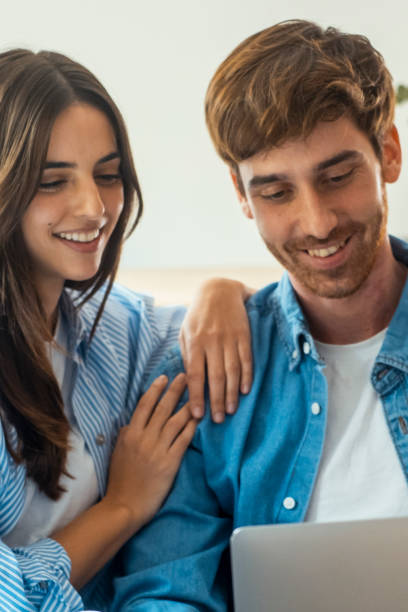 istock Young married couple sitting on sofa in the living room at home using tablet PC for internet and social media. Happy family resting on couch enjoying weekend watching video or talking on video call. 2124492989