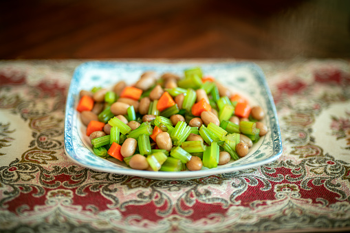 On the dining table, in a plate, celery and boiled peanuts are mixed together with salt, creating a delicious and refreshing dish.