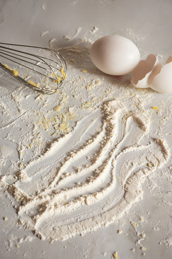 The ingredients for baking - flour, eggs, and whisk on a wooden surface.