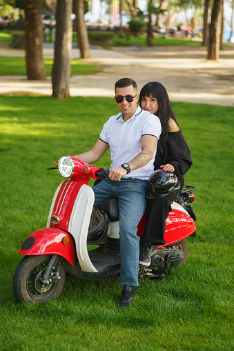 Cute young couple riding motor scooter at park