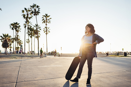 Woman walking on Venice Beach promenade going to skate at sunset.