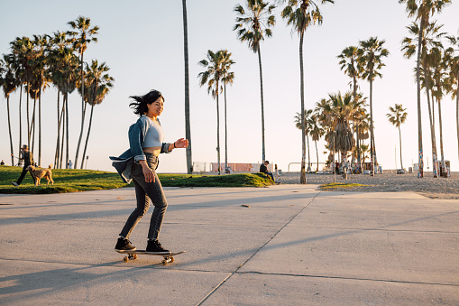 Young woman with skateboard in Venice Beach enjoying a beautiful sunset evening.