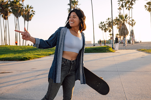 Young woman with a skateboard walking by the beach promenade and meet friends.