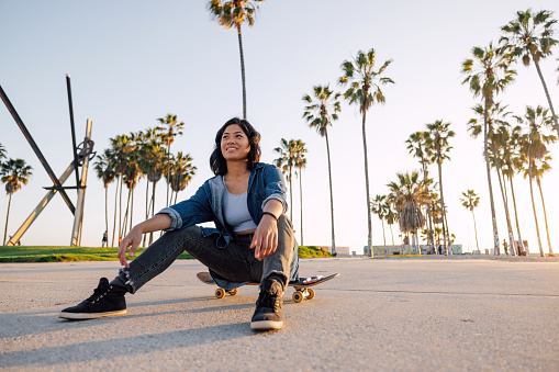 Woman walking on Venice Beach promenade going to skate at sunset.