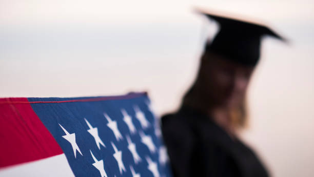 istock Graduate in robe holds U.S. flag 2124615408