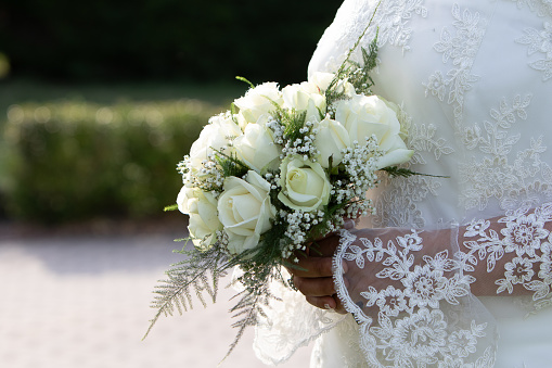 a delicate close-up captures a bride's lace-sleeved arm cradling a bouquet of white roses, symbolizing elegance and a timeless wedding tradition
