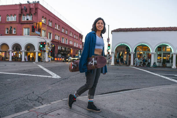 Young woman walk back home from Venice beach with her skateboard at dusk.