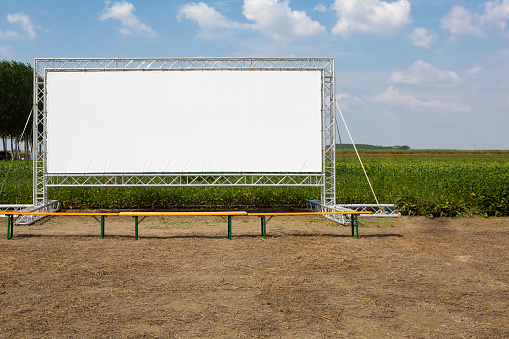 A vast, empty cinema screen stands prominently in a rural setting, offering an ideal advertising space for marketers