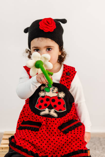 Tiny little girl in ladybug costume smelling artificial chamomile flower in studio.