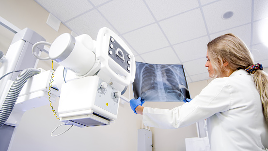Doctor with x-ray of lungs in hands in modern medical radiology hospital. The doctor analyzes the condition of the lungs. The virus attacks the lungs. COVID-19 and medical examinations.