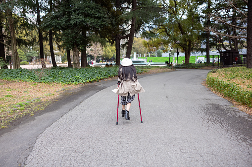 Rear view of little girl walking on crutches in public park