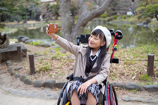Little girl on wheelchair taking selfie pictures in public park