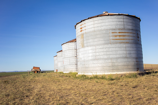 rural landscape with metal silos standing tall in a grain field with large-capacity storage. Nearby, an old, rusted water cart