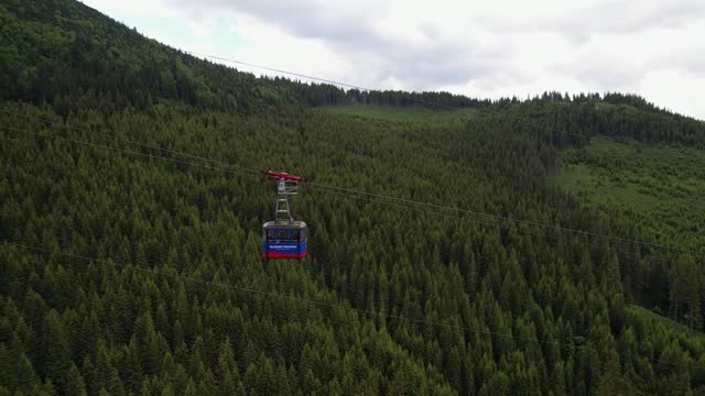 A cable car gliding over lush green forest canopy, cloudy sky backdrop, tranquil mountain scenery, aerial view