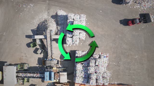 Aerial of machines working at a recycling facility with a rotating recycle icon