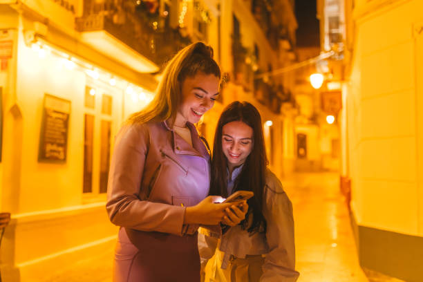 istock Two beautiful young woman looking at their phone while outside at night 2124796390
