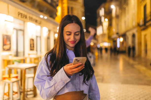 istock Beautiful young woman using her smart phone while outdoors at night 2124796902