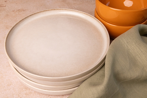 Beige plates, orange bowls and a green towel on a brown stone tabletop.