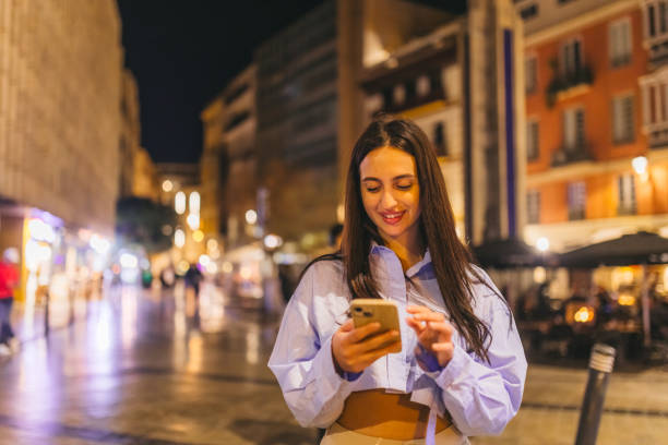 istock Beautiful young woman using her smart phone while outdoors at night 2124797436