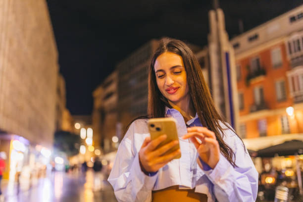 istock Beautiful young woman using her smart phone while outdoors at night 2124797437