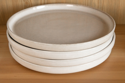 A stack of four beige ceramic dinner plates in a wooden cupboard.