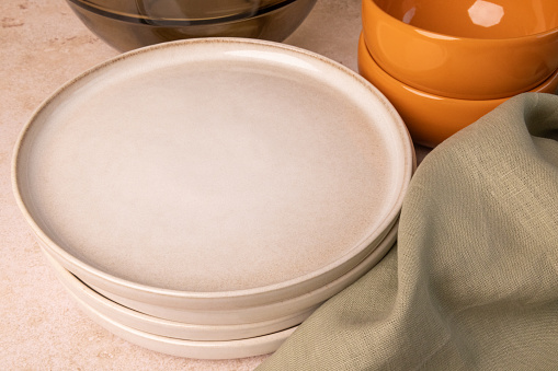 Beige plates, orange bowls and a green towel on a brown stone tabletop.