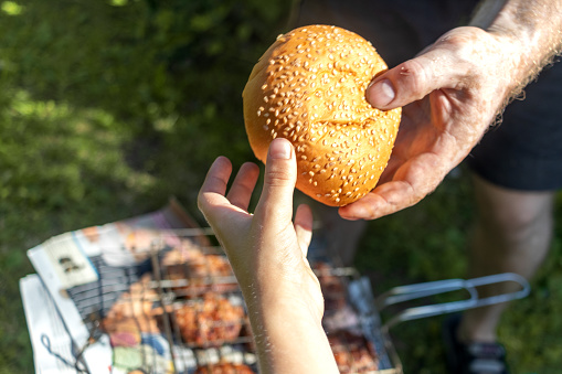 Father gives his son bread. Sesame bun. Close-up of hands. Quotes from Holy Scriptures. Summer picnic, vacation in nature. Family values.