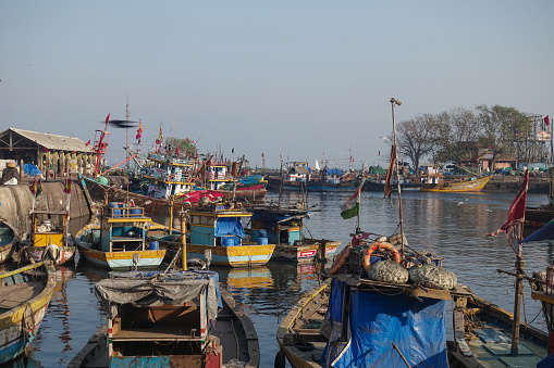 Fishing boats moor in the harbor while seagulls and crows fly around in Sassoon Docks which is one of the oldest docks in Mumbai and was the first wet dock constructed, It is one of largest fish markets in Mumbai City