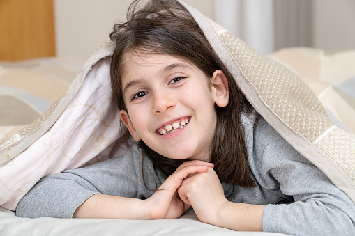 Smiling little girl hiding under blanket in bed after shower.