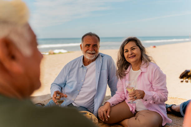 istock Senior friends talking and drinking wine on beach picnic 2124939093
