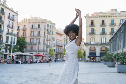 A young woman of mixed race raising her arms happily in the middle of the square