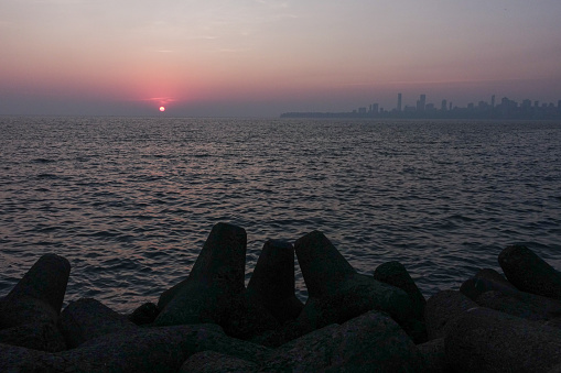 Sunset over the Arabian Sea next to Mumbai's cityscape viewed from Marine Drive with Tetrapod-shaped rock Groyne in the foreground